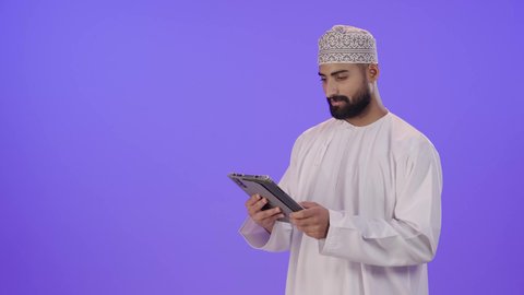تصفح مواقع التواصل الاجتماعي, استخدام التكنولوجيا والتقنيات الحديثة، متابعة الأفلام والمسلسلات الممتعة، المحادثة مع الأهل والأصدقاء، رجل عربي خليجي عماني يرتدي الدشداشة و الكمة  يحمل بيده جهاز التابلت,ايماءات الاندماج و التركيز