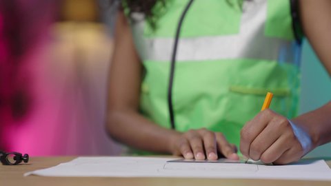 أدوات وأجهزة للعمل في التصميم الهندسي، تصويرمقرب ليد بنت عربية خليجية سعودية سمراء ترتدي سترة حماية خاصة بالعمل الهندسي تجلس على الطاوله امام جهاز التابلت ترسم بالفرجار على مخطط تصميم هندسي  ، مهن ووظائف هندسية