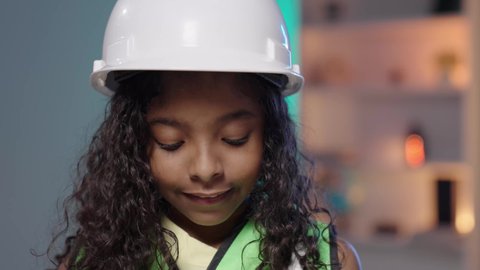 تقديم مفاهيم الهندسة والمهن المستقبلية للأطفال، تصوير مقرب لفتاه عربية خليجية سعودية سمراء ترتدي خوذة الوقاية الخاصة بالعمل و ستره الحماية الهندسي تنظر الى الاسفل، مهن ووظائف هندسية