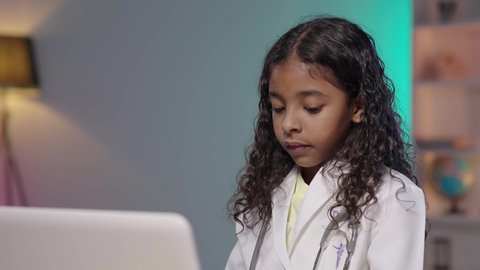 تحديد واختيار مهنة المستقبل منذ الصغر، مفهوم الطب والرعاية الصحية، إستخدام أجهزة تقنية حديثة، تصويرمقرب لبنت عربية خليجية سعودية سمراء ترتدي المعطف الطبي و السماعات الخاص بمهنة الطبيب تقوم بإدخال البيانات الطبية في جهاز الحاسوب المحمول