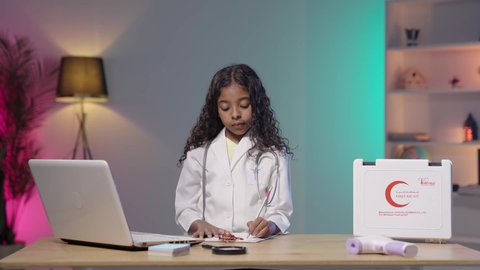 تدوين نتائج الفحوصات بالسجل الطبي، تصوير لبنت عربية خليجية سعودية  ترتدي المعطف الطبي و السماعات الخاص بمهنة الطبيب تجلس على الطاوله امام الحاسب المحمول تقوم بإعداد التقارير الطبية و الإحصاءات ، مهن و وظائف مستقبلية ، خلفية بيضاء