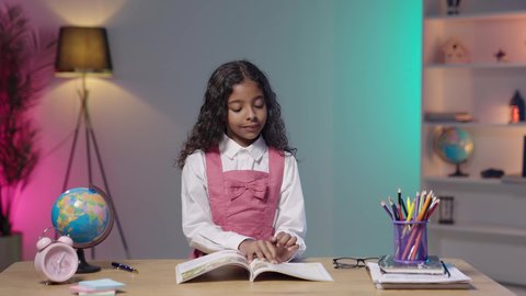 Back to school, education in the schools of the Kingdom of Saudi Arabia, an Arab Gulf Saudi girl wearing a school uniform sitting at a study table reviewing lessons and doing homework, supplies and textbooks.