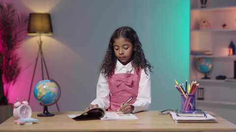 المقررات والمناهج التعليمية الحديثة والمطورة، موسم العودة للمدارس، مفهوم الاجتهاد وطلب التفوق، بورتريه مقرب لبنت بنت عربية خليجية سعودية ترتدي الزي المدرسي تجلس على طاوله تقوم بكتابة شيء ما، مذاكره الدروس المدرسيه