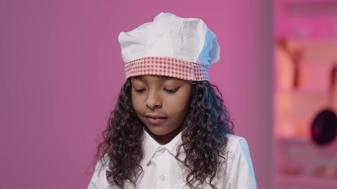 Learn cooking skills and culinary arts, gestures of integration and focus, a close-up shot of a Saudi Arabian Gulf girl with a dark complexion wearing a chef's uniform looking down, future careers and jobs.