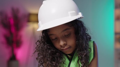 تعريف الأطفال على مفهوم الهندسة والمهن المستقبلية، تصوير مقرب لفتاه عربية خليجية سعودية سمراء  ترتدي خوذة الوقاية الخاصة بالعمل و ستره الحماية الهندسي تنظر الى الاسفل، مهن ووظائف هندسية