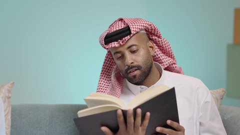 الشغف في ممارسة هواية المطالعة، دعم وتنمية الذخيرة اللغوية والعلمية، قضاء أوقات ممتعة في قراءة الكتب والقصص والروايات، بورتريه مقرب لرجل عربي خليجي سعودي مثقف يرتدي الثوب و الشماغ يقوم بتصفح كتاب، مفهوم التعلم الذاتي والاطلاع والثقافة، خلفية زرقاء