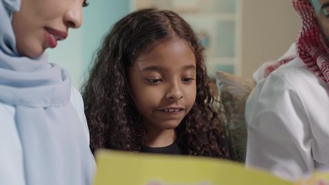 هواية المطالعة والاستكشاف، قضاء وقت الفراغ بالتعلم والثقافة، مفهوم التثقيف والبحث العلمي، بورتريه مقرب لبنت عربيه خليجيه سعودية ترتدي الزي الكاجوال تجلس برفقه والدتها تقوم بقراءة كتاب ، تنمية مهرات الطفل، شرح وتفسير أحداث القصة بأسلوب شيق وممتع، خلفية زرقاء