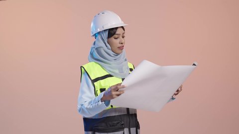 مهنة ووظيفة نسائية سعودية، التحقق من تنفيذ المشروع الإنشائي، مفهوم الهندسة والإنشاء المعماري, بورتريه لمهندسة عربية خليجية سعودية محجبة ترتدي العباءة والسترة و خوذة الحماية تمسك بيدها المخطط الهندسي، خلفية وردية