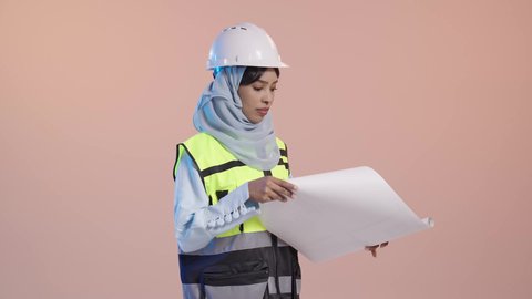مفهوم الهندسة والإنشاء المعماري، التحقق من تنفيذ المشروع الإنشائي, مهنة ووظيفة نسائية سعودية, بورتريه  لمهندسة عربية خليجية سعودية محجبة ترتدي العباءة والسترة و خوذة الحماية تمسك بيدها المخطط الهندسي، خلفية وردية