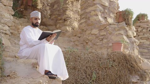 اكتساب المعرفة وتنمية الذخيرة اللغوية والعلمية، قضاء وقت ممتع في قراءة الكتب والروايات، شاب عربي خليجي عماني مثقف يرتدي الدشداشة والكمة يجلس في إحدى الحدائق العامة يقوم بقراءة كتاب، مفهوم التعلم الذاتي والاطلاع والثقافة، الشغف في ممارسة هواية المطالعة