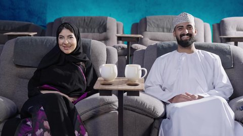 مشاهدة فيلم سينمائي داخل قاعة السينما، تقوية علاقة الأزواج من خلال قضاء أوقات ودودة وممتعة، الاستمتاع بمشاهدة المباريات في عطلة نهاية الأسبوع، زوجان عربيان خليجيان عمانيان زوجة ترتدي الحجاب والعباءة تجلس في السينما مع زوجها، نزهات الأصدقاء لقضاء أوقات ممتعة