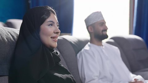 الأزواج داخل قاعات السينما، مشاهدة فيلم سينمائي داخل قاعة السينما، قضاء أوقات ممتعة، الاستمتاع بمشاهدة المباريات في عطلة نهاية الأسبوع، زوجان عربيان خليجيان عمانيان زوجة ترتدي الحجاب والعباءة تجلس في السينما مع زوجها، نزهات الأصدقاء لقضاء أوقات ممتعة