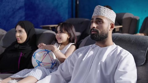 بناء علاقات اجتماعية ناجحة، مشاهدة فيلم سينمائي داخل قاعة السينما، قضاء أوقات ممتعة ومسلية، الاستمتاع بمشاهدة المباريات في عطلة نهاية الأسبوع، عائلة عربية خليجية عمانية أم ترتدي الحجاب والعباءة تجلس في السينما مع زوجها وطفلتها، نزهات الأصدقاء لقضاء أوقات ممتعة