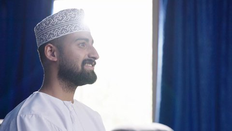 مشاهدة فلم سينمائي، تصوير مقربة  لرجل عربي خليجي عماني يرتدي الثوب التقليدي يجلس على الكنبة ينظر إلى مكان ما بايماءات السعادة والسرور، انشطة ترفيهية خارجية، تعابير الاندماج والتركيز، الشغف في ممارسة الهوايات، متابعة برامج التلفاز، قضاء وقت ممتع في خارج المنزل