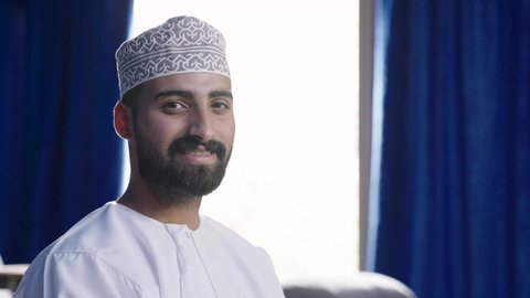 قضاء وقت ممتع في خارج المنزل، مشاهدة فلم سينمائي، تصوير مقربة  لرجل عربي خليجي عماني يرتدي الثوب التقليدي يجلس على الكنبة ينظر إلى مكان ما بايماءات السعادة والسرور، انشطة ترفيهية خارجية، تعابير الاندماج والتركيز، الشغف في ممارسة الهوايات، متابعة برامج التلفاز