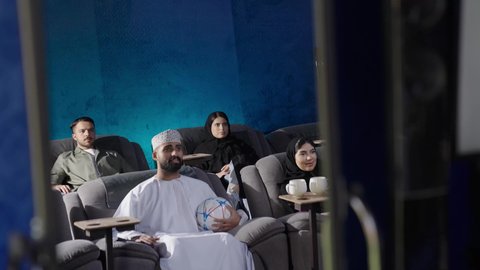 قضاء أوقات ممتعة ومسلية،  الاستمتاع بمشاهدة المباريات في عطلة نهاية الأسبوع،بناء علاقات اجتماعية ناجحة،تصوير مقرب إمرأة عربية خليجية عمانية ترتدي الحجاب والعباءة تجلس في السينما، مشاهدة فيلم سينمائي، نزهات الأصدقاء معا لقضاء أوقات ممتعة
