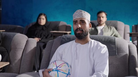 لاستمتاع بمشاهدة المباريات في عطلة نهاية الأسبوع، نزهات الأصدقاء معا لقضاء أوقات ممتعة ،بناء علاقات اجتماعية ناجحة، إمرأة عربية خليجية عمانية ترتدي الحجاب والعباءة تجلس في السينما ترفع يديها بإيماءات البهجة والسرور، مشاهدة فيلم سينمائي، قضاء أوقات ممتعة ومسلية