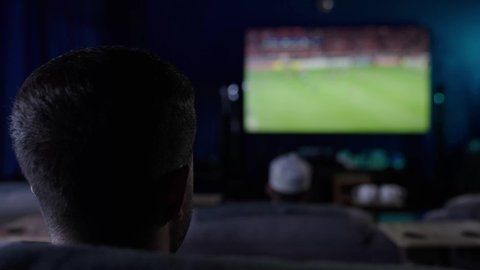 ايماءات الفوز والانتصار ، الشغف بالانشطة الترفيهية، مشاهدة المباراة والحماس ,  المباريات والألعاب الرياضية، رجل عربي خليجي عماني يرتدي الزى التقليدى يجلس على أريكة مريحة ، المشاهدة بتعابير التركيز والاندماج ، متابعة مباراة كرة القدم .