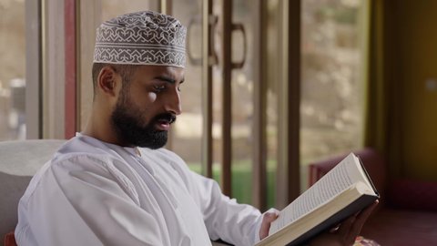 قضاء أوقات ممتعة في قراءة الكتب والقصص والروايات، جلسة في إحدى الشاليهات الخارجية، الشغف في ممارسة هواية المطالعة، دعم وتنمية الذخيرة اللغوية والعلمية، تصوير مقرب لشاب عربي خليجي عماني مثقف يقوم بتصفح كتاب، مفهوم التعلم الذاتي والاطلاع والثقافة