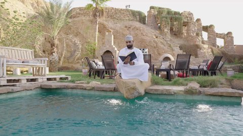 مراجعة البحوث العلمية، قضاء وقت ممتع في قراءة الكتب والروايات، تنمية الذخيرة اللغوية والعلمية، شاب عربي خليجي عماني مثقف يرتدي الدشداشة والكمة يجلس في إحدى الحدائق العامة يقوم بقراءة كتاب، مفهوم التعلم الذاتي والاطلاع والثقافة، الشغف في ممارسة هواية المطالعة