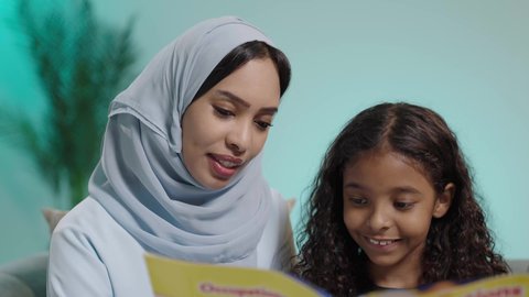 شرح وتفسير أحداث القصة بأسلوب شيق وممتع، قضاء وقت الفراغ بالتعلم والثقافة، هواية المطالعة والاستكشاف، مفهوم التثقيف والبحث العلمي، بورتريه لإمرأة عربية خليجية عمانية ترتدي العباءة وتجلس تقوم بقراءة كتاب لطفلتها، تنمية مهرات الطفل، خلفية زرقاء
