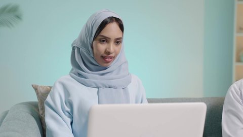 ايماءات الاندماج والتركيز، إنجاز مهام العمل عن بعد، التسوق الالكتروني وطلبات الاونلاين ، دردشة ومحادثات و تواصل اجتماعي ، اجراء اجتماع عمل عبر الانترنت، بورتريه لسيدة عربية عمانية خليجية تجلس على كرسي مريح وتستخدم الحاسوب المحمول، خلفية زرقاء