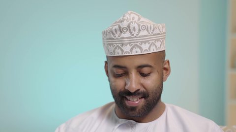 Chatting and conversations and social communication, completing remote work tasks, gestures of engagement and focus, online shopping and online orders, conducting a business meeting via the internet, a close-up portrait of an Arab Omani Gulf man sitting in a comfortable chair and using a mobile phone, blue background.