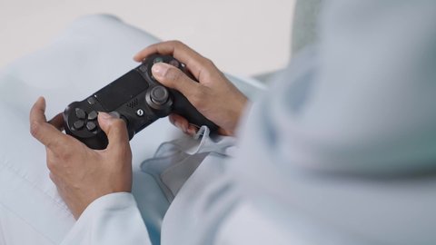 استخدام التقنيات الحديثة في التسلية وقضاء الأوقات الترفيهية، المتعة والتسلية  بألعاب البلايستيشن الترفيهية، قضاء وقت ممتع بلعب ألعاب الفيديو، بورتريه مقرب لإمرأة عربية خليجية عمانية تجلس  تمسك عصا التحكم وتلعب بألعاب الفيديو، خلفية زرقاء