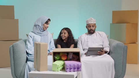 الاستمتاع بقضاء وقت مع الابناء، جلسة عائلية سعيدة، التسامر وتبادل الاحاديث، تعابير المودة والمحبة،بورتريه لعائلة عربية خليجية عمانية تجلس على آريكة يتناقشون ويتحدثون ام واب يرتدون الزي التقليدي ، التسلية والترفيه في العطلة، صناديق وكراتين، خلفية زرقاء