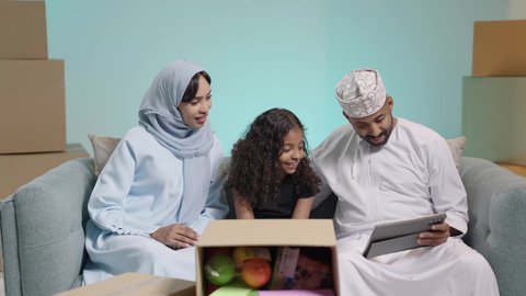 الاستمتاع بقضاء وقت مع الابناء، جلسة عائلية سعيدة، التسامر وتبادل الاحاديث، تعابير المودة والمحبة،بورتريه مقرب لعائلة عربية خليجية عمانية تجلس على آريكة يتناقشون ويتحدثون ام واب يرتدون الزي التقليدي ، التسلية والترفيه في العطلة، صناديق وكراتين، خلفية زرقاء