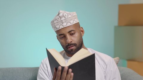 الشغف في ممارسة هواية المطالعة، دعم وتنمية الذخيرة اللغوية والعلمية، قضاء أوقات ممتعة في قراءة الكتب والقصص والروايات، بورتريه مقرب لرجل عربي خليجي عماني مثقف يرتدي الدشداشة والكمة يقوم بتصفح كتاب، مفهوم التعلم الذاتي والاطلاع والثقافة، خلفية زرقاء