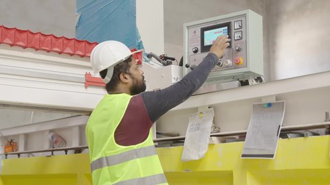 دمج التكنولوجيا الحديثة في المصانع، العمل في المجال الصناعي والتقني، تصوير من الخلف لعامل عربي خليجي سعودي يرتدي الخوذة و ستره الحماية يستخدم شاشة اللمس داخل مصنع الرخام