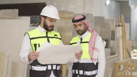 الإشراف على تقدم المشاريع ومراقبة سير العمل، تصويرمقرب لمهندس عربي خليجي سعودي يرتدي سترة وخوذة الحماية يحمل مخطط هندسي برفقة زميله، الاشراف على سير خطة العمل، معامل ومصانع  محليه سعوديه، حوارات ونقاشات هادفة