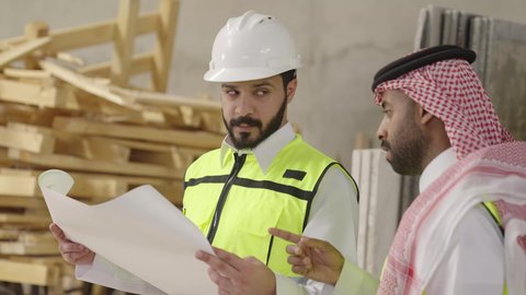 مناقشات هادفة لتبادل الأفكار، تصويرمقرب لمهندس عربي خليجي سعودي يرتدي سترة وخوذة الحماية يحمل مخطط هندسي برفقة زميله، الاشراف على سير خطة العمل، معامل ومصانع  محليه سعوديه، الإشراف على العمليات الصناعية اليومية