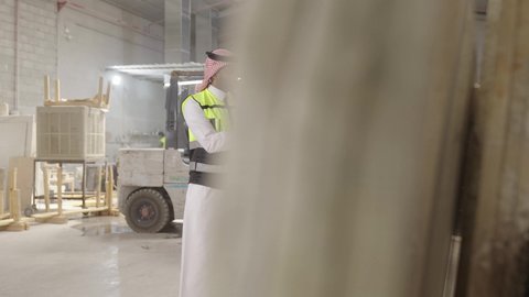 متابعة مراحل التصنيع داخل المصنع، ارتداء خوذة الحمايه ، تصوير لمهندسان عربيان سعوديان خليجيان يرتديان الثوب يقومان بمناقشة العمل في احدى المستودعات ، معامل ومصانع محليه سعوديه، تسجيل و تدوين الملاحظات