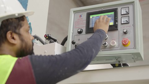 Working in the industrial and technical field, integrating modern technology in factories, a close-up shot from behind of an Arab Gulf Saudi worker wearing a helmet and safety vest using a touchscreen inside a marble factory.