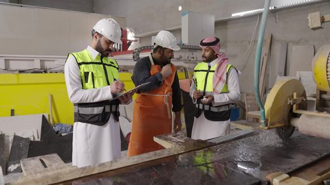 تدوين وتسجيل الملاحظات والمعلومات ، تحقيق الثورة الصناعية، التعاون في أداء المهام، مجموعة من المهندسين الصناعيين العرب السعوديين الخليجيين يرتدون ملابس العمل وخوذة الحماية يتابعان سير أعمال المصنع ، جودة الانتاج والتصنيع، مهن ووظائف سعودية