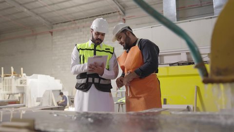 متابعه سير أعمال المصنع، مفهوم الاشراف على الانتاجية، مهندس عربي خليجي سعودي يرتدي سترة وخوذة الحماية يحمل بيده حافظة ورقية يقف برفقة عامل، جودة الانتاج والتصنيع، تحقيق الثورة الصناعية، مهن ووظائف سعودية
