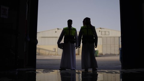 تصوير ظلي لمهندسان عربيان سعوديان خليجيان يرتديان الثوب يقومان بالمشي  في احدى المستودعات ، ارتداء خوذة الحمايه في المصنع ، معامل ومصانع  محليه سعوديه