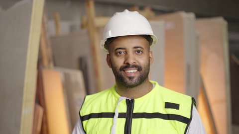 العمل في القطاع الهندسي، مهن ووظائف سعودية، تصوير لمهندس عربي خليجي سعودي مبتسم يرتدي الخوذة وسترة الحماية يقف بأيدي متقاطعه في موقع العمل ينظر إلى الكاميرا بإيماءات السرور