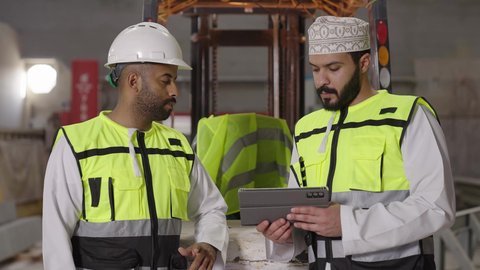 استخدام جهاز التابلت في الأعمال الهندسية، مهن ووظائف عمانية، متابعة سير العملية الإنتاجية في المصانع, التطور في الإنتاج والتصنيع وتحقيق الثورة الصناعية, التحول التقني والتكنولوجي الحديث, مهندسان عربيان خليجيان عمانيان يرتديان سترة الحماية يتحاوران ويتناقشان في مواضيع العمل
