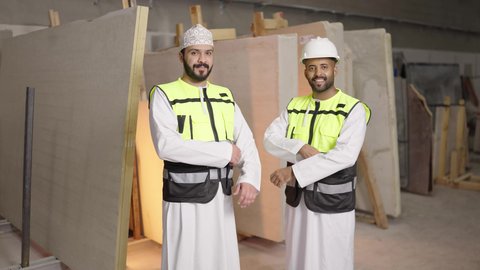 ورشات عمل ومهن تقليدية، الوقوف والنظر إلى الكاميرا بايدي متقاطعه بإيماءات الثقة بالنفس والجدية, مصانع ومعامل في سلطنه عمان, تصوير لمهندسان عربيان خليجيان عمانيان يرتديان سترة الحماية يعملان في مصنع رخام, الاشراف على سير خطة العمل