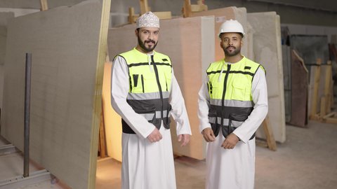 الوقوف والنظر إلى الكاميرا بايدي متقاطعه بإيماءات الثقة بالنفس والجدية, ورشات عمل ومهن تقليدية , مصانع ومعامل في سلطنه عمان, تصوير لمهندسان عربيان خليجيان عمانيان يرتديان سترة الحماية يعملان في مصنع رخام, الاشراف على سير خطة العمل