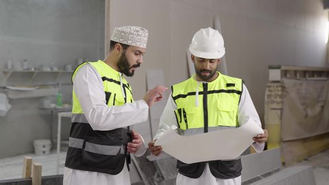 مناقشات هادفة لتبادل الأفكار، مصنع تصنيع الرخام، تصوير لمهندس عربي خليجي عماني يرتدي سترة وخوذة الحماية يحمل مخطط هندسي برفقة زميله ، الاشراف على سير خطة العمل، حرف ومهن يدوية شعبية