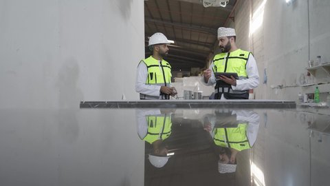 متابعة إجراءات العمل عبر التابلت، استخدم شريط القياس لقياس ألواح الرخام، تصوير لمهندسان عربيان خليجيان عمانيان يرتديان الستراة العاكسة وخوذة الحماية داخل مصنع الرخام يقومان بالإشراف والنقاش في العمل