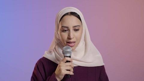 العمل في تقديم الفقرات و البرامج الفنية، إلقاء المحاضرات وإقامة الندوات، بورتريه مقرب لامراة عربية خليجية سعودية محجبه ترتدي العباءة تحمل بيدها الميكروفون , خلفية ملونه