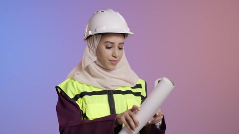 مهن ووظائف نسائية، مفهوم الهندسة وأعمال البناء, بورتريه لمهندسة عربية خليجية سعودية محجبة ترتدي عباءة سوداء مع السترة وخوذة الحماية تقوم بدراسه وتصفح المخططات الهندسيه، العمل في القطاع الهندسي في السعودية, خلفية ملونه