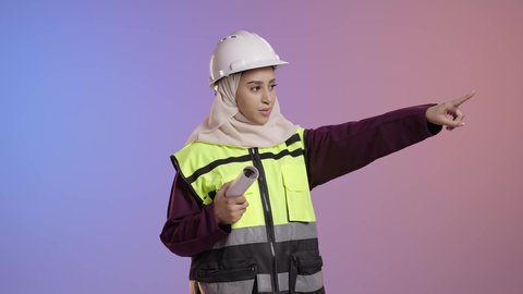 حمل المخطط الهندسي، دور الهندسة الإنشائية في تطور المجتمع السعودي،, بورتريه لمهندسة عربية خليجية سعودية مسلمة محجبة ترتدي الخوذة البيضاء وسترة الحماية تشير الى شيء ما، خلفية ملونه
