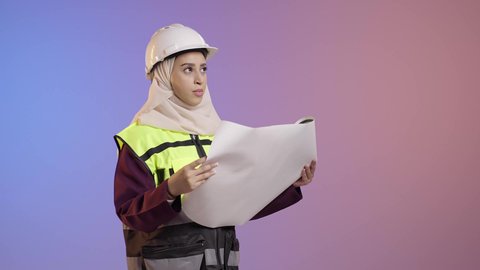 النظر الى شيء ما، مفهوم الهندسة وأعمال البناء, بورتريه لمهندسة عربية خليجية سعودية محجبة ترتدي عباءة سوداء مع السترة وخوذة الحماية تقوم بدراسه وتصفح المخططات الهندسيه، مهن ووظائف نسائية، العمل في القطاع الهندسي في السعودية, خلفية ملونه