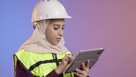 الأجهزة التقنية الحديثة، التأكد من سير الأعمال بالشكل المطلوب والصحيح، كتابة آخر المستجدات حول المشروع، بورتريه مقرب لمهندسة عربية خليجية سعودية ترتدي الحجاب والخوذة وسترة الحماية تقوم باستخدام الجهاز اللوحي، تدوين و تسجيل الملاحظات, خلفية ملونه